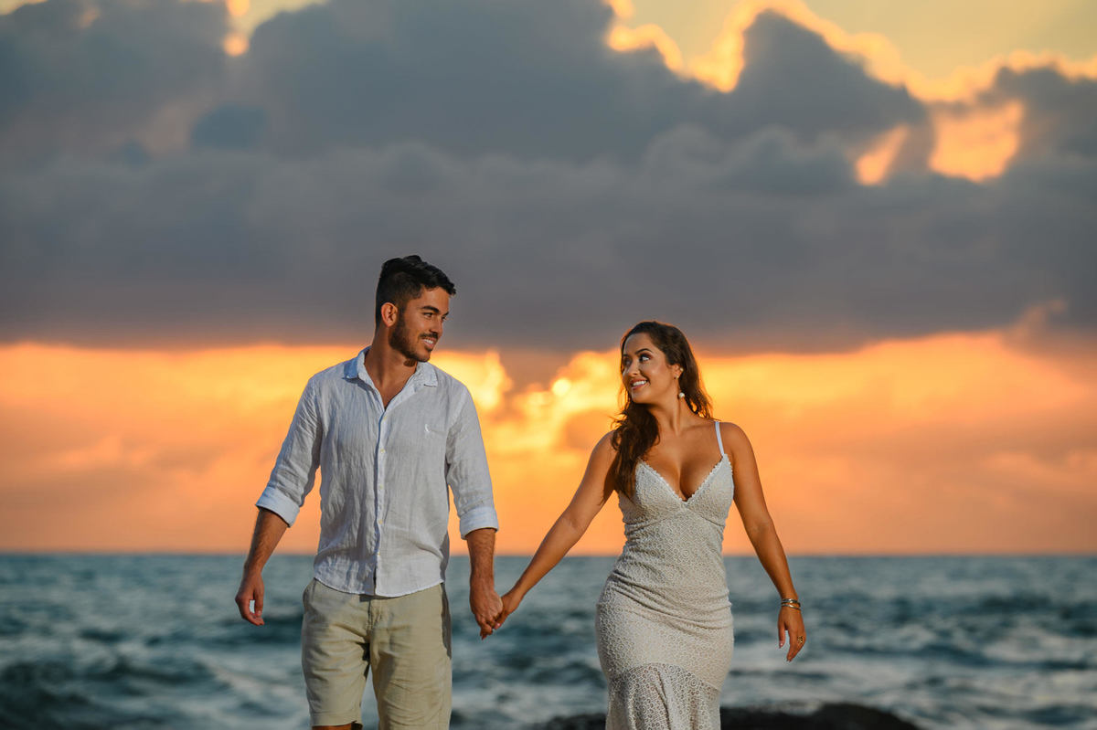 Casal caminhando de mãos dadas na Praia do Estaleirinho ao nascer do sol