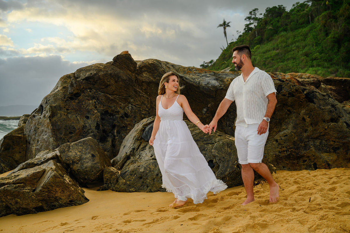 Casal caminhando de mãos dadas na praia durante ensaio pré-wedding em Balneário Camboriú