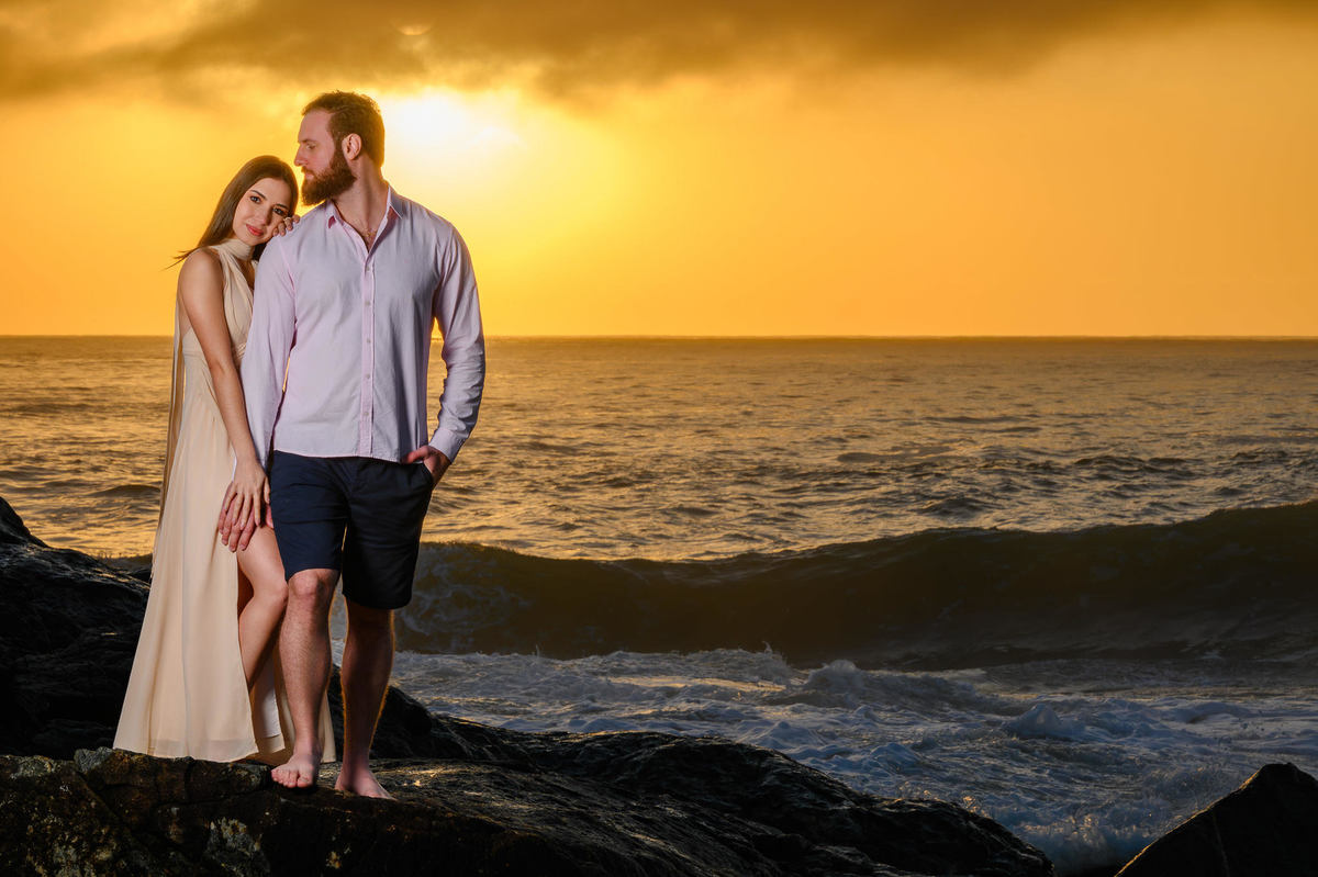 Casal em contraluz com o sol refletindo no mar durante ensaio pré-casamento na praia