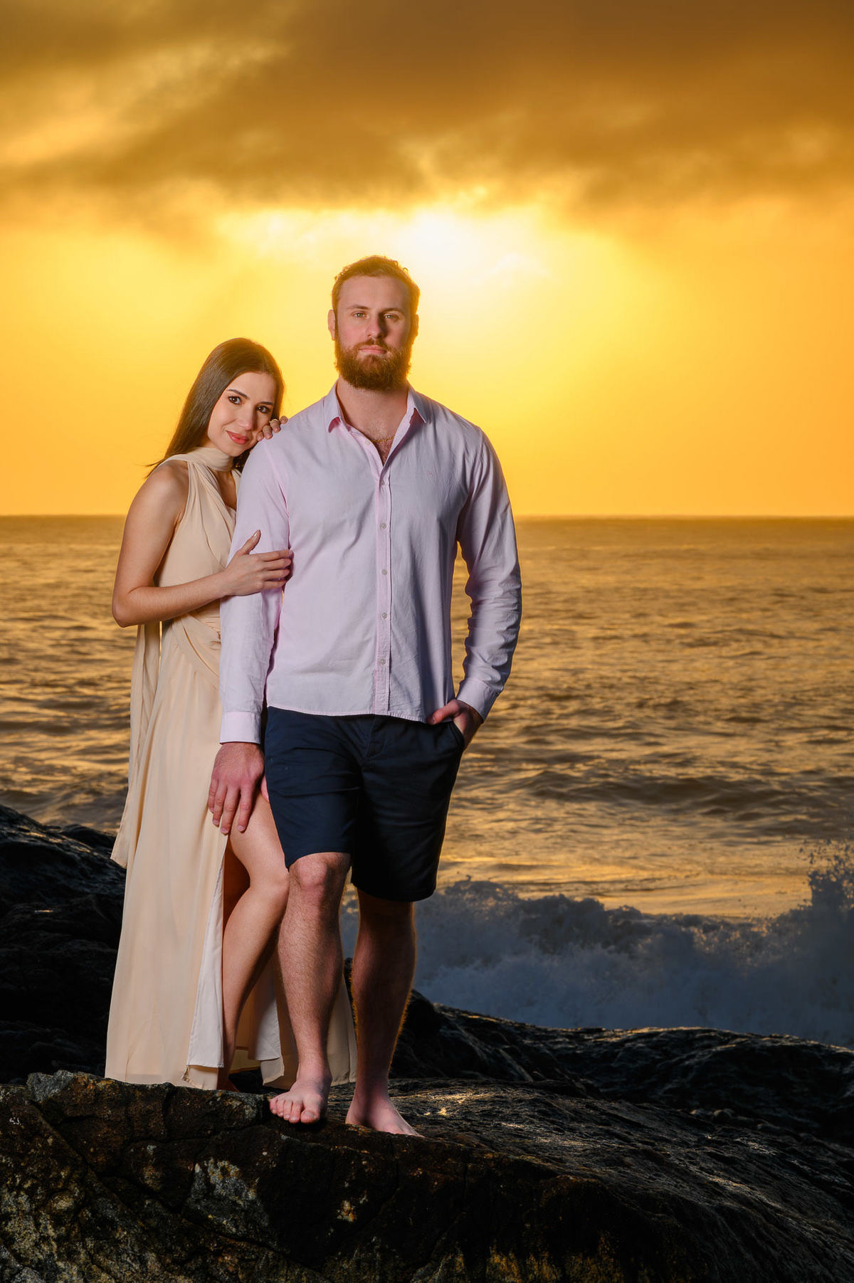 Casal em contraluz com o sol refletindo no mar durante ensaio pré-casamento na praia