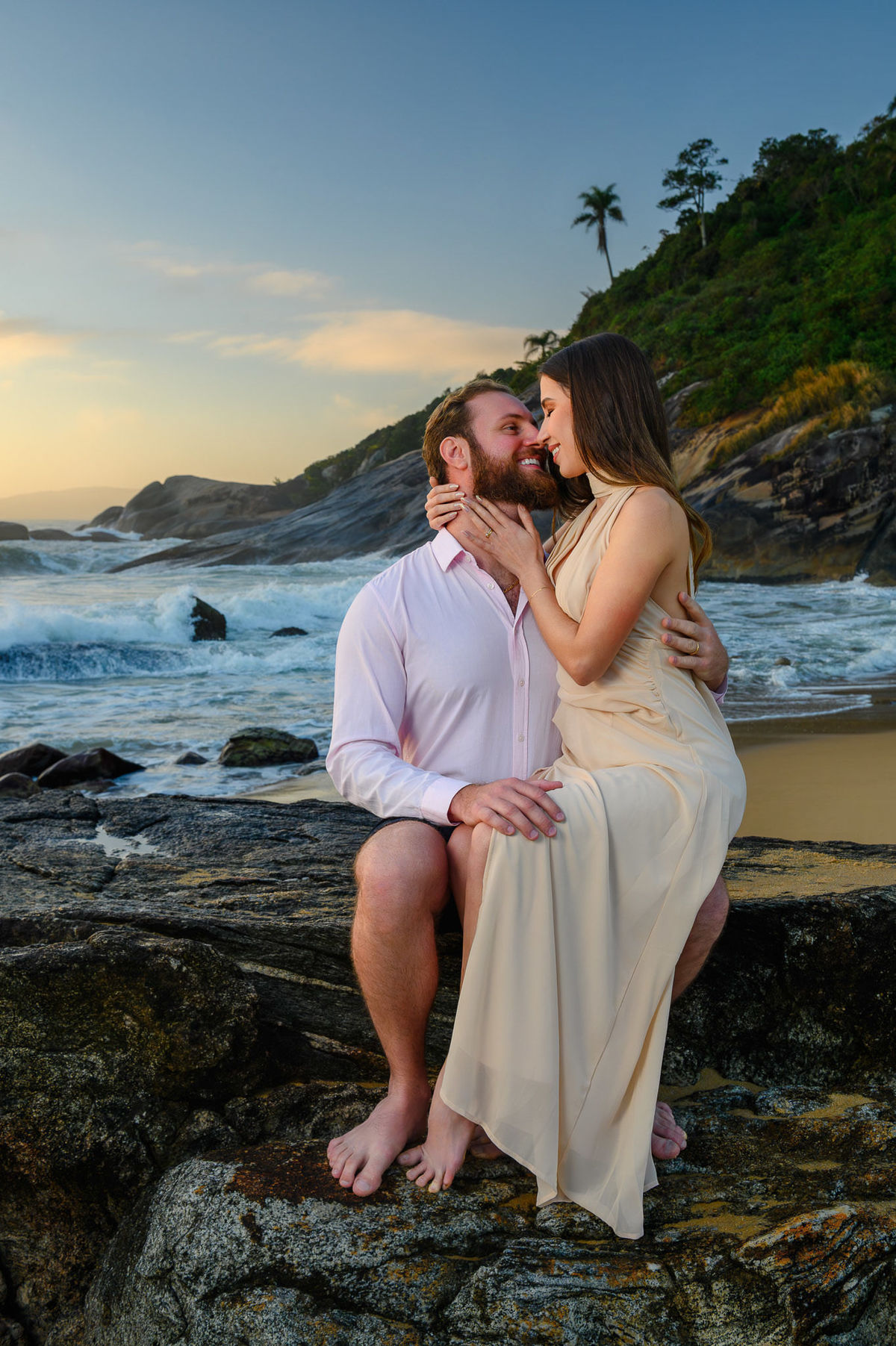 Ensaio pré-wedding com casal sentado nas pedras e ondas do mar em Balneário Camboriú