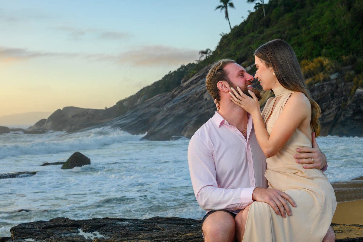 Ensaio pré-wedding com casal sentado nas pedras e ondas do mar em Balneário Camboriú