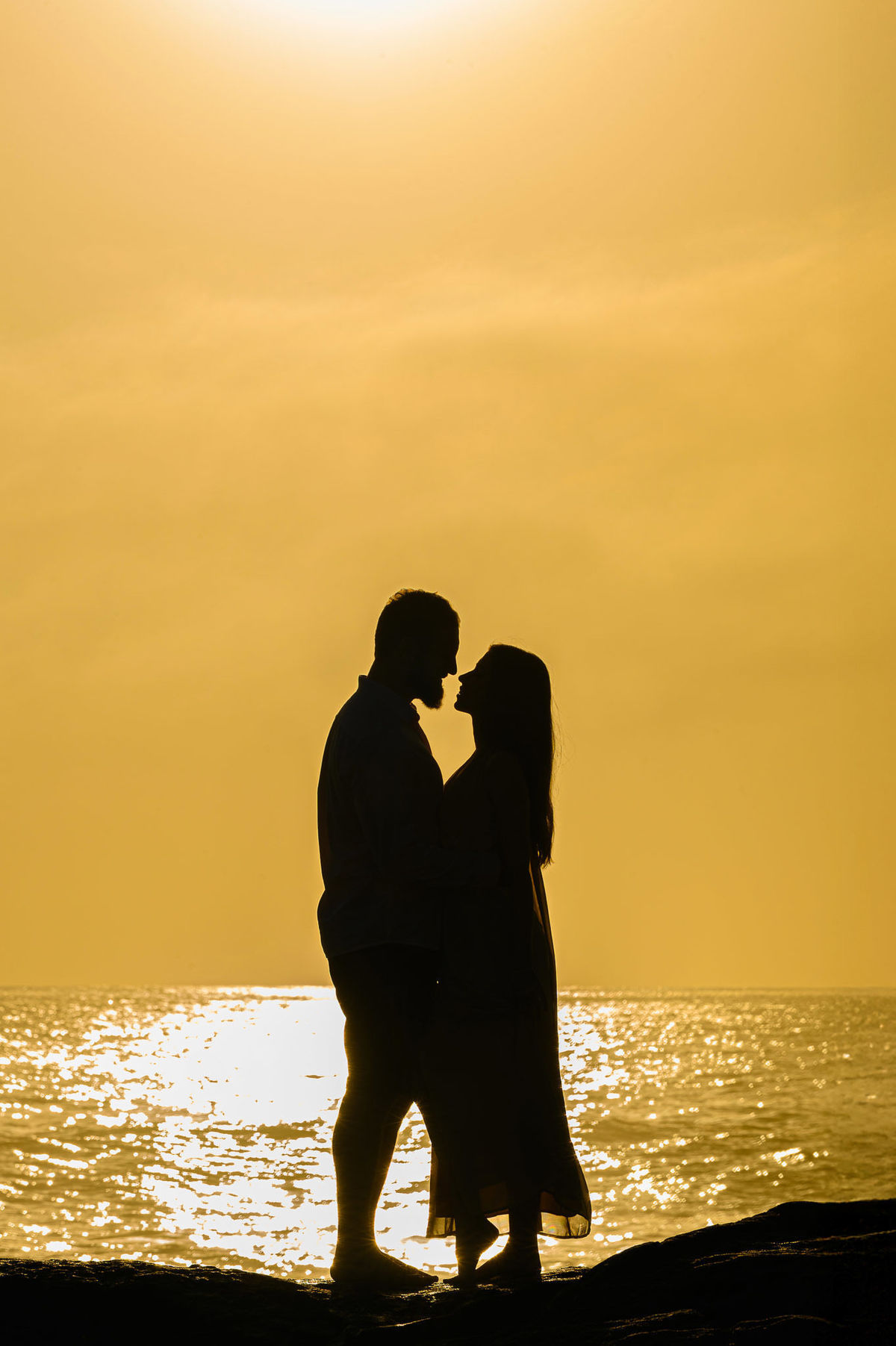 Casal em silhueta na beira do mar com o sol nascendo em Balneário Camboriú