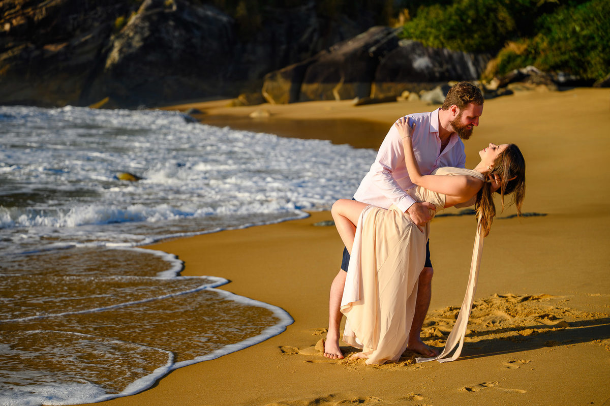 Casal em pose romântica na beira do mar com ondas ao fundo na Praia do Estaleirinho