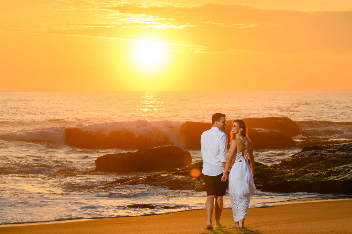 Casal caminhando pela areia com o sol nascendo atrás no ensaio pré-wedding em Balneário Camboriú – SC