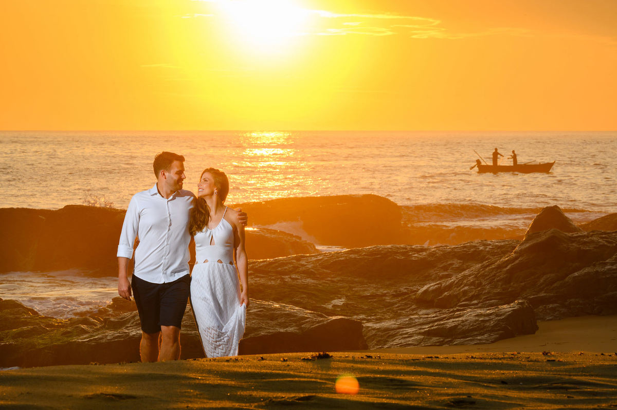 Casal caminhando pela praia com barco ao fundo no amanhecer em Balneário Camboriú – SC