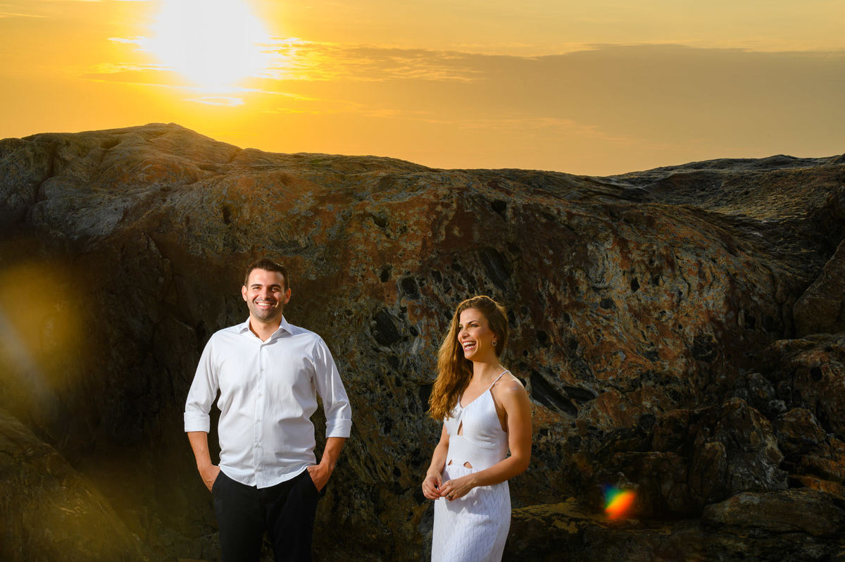 Casal sorrindo em frente às pedras iluminadas pelo sol nascente em Balneário Camboriú – SC