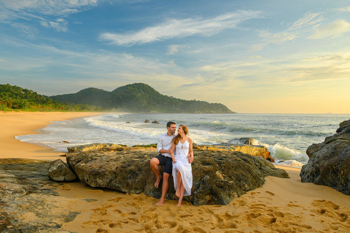 Casal sentado sobre pedras com paisagem da praia ao fundo em ensaio pré-wedding em Santa Catarina