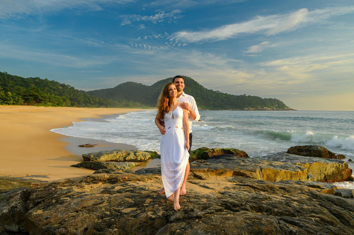 Casal sentado sobre pedras com paisagem da praia ao fundo em ensaio pré-wedding em Santa Catarina