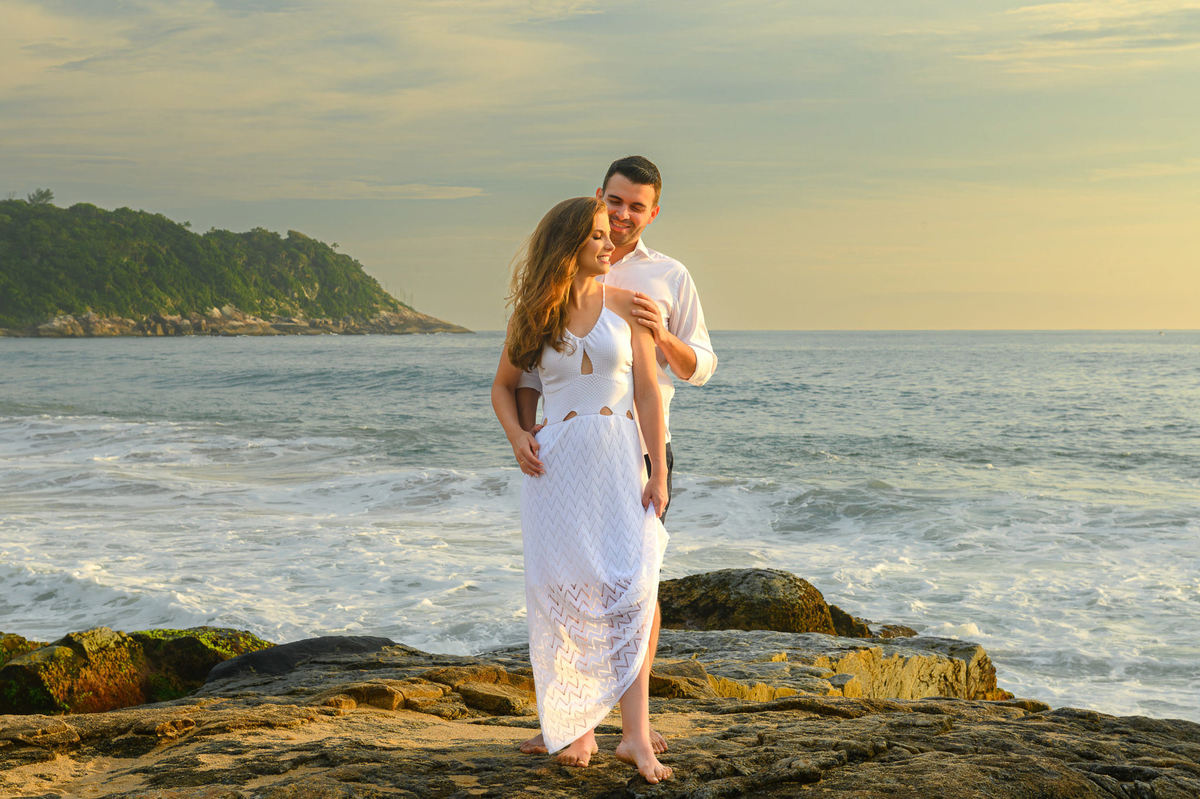 Casal sentado sobre pedras com paisagem da praia ao fundo em ensaio pré-wedding em Santa Catarina