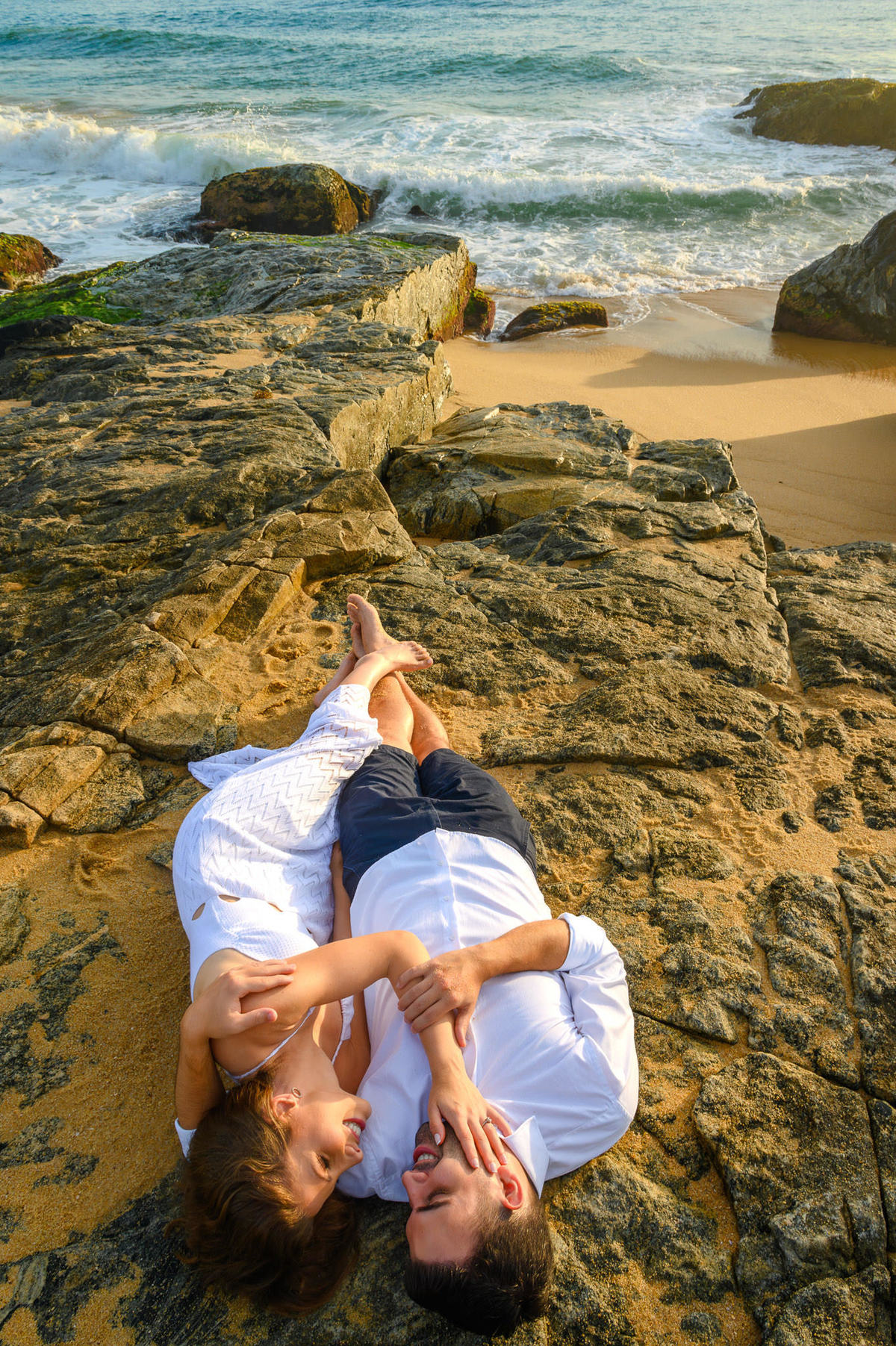 Casal deitado sobre as pedras durante ensaio pré-wedding ao amanhecer em Balneário Camboriú – SC