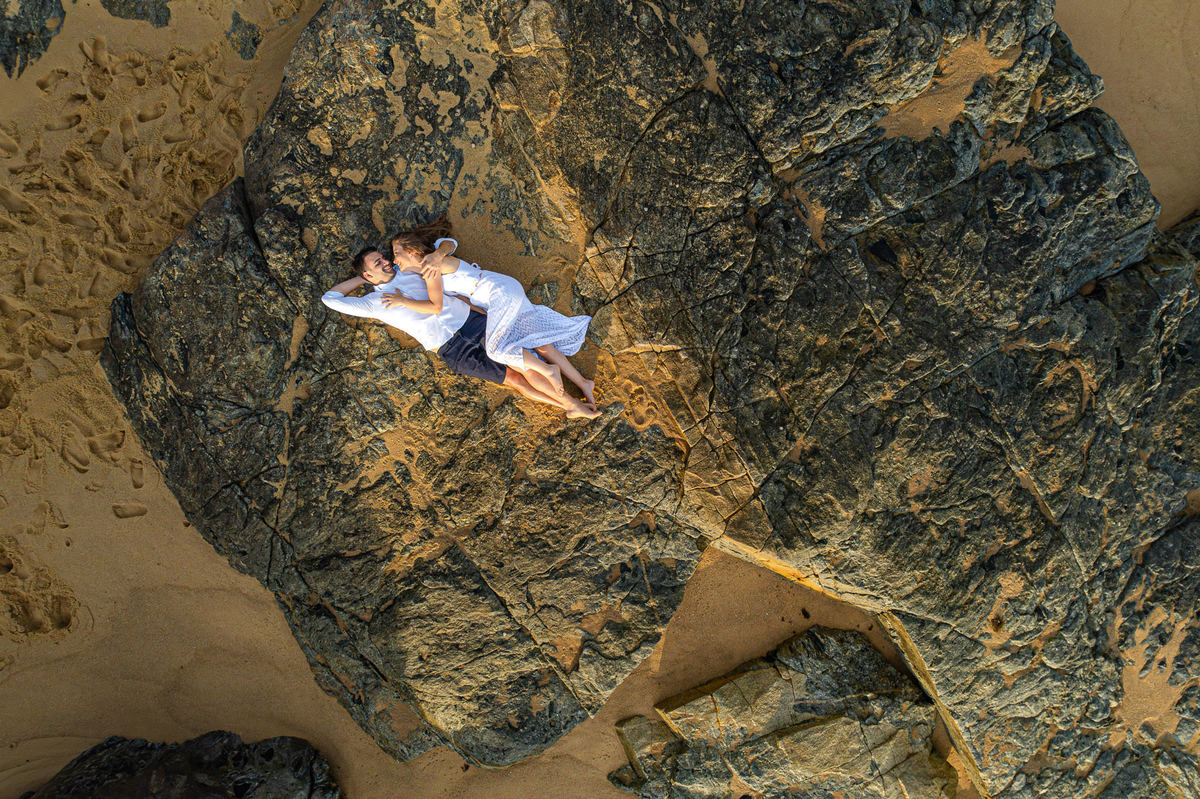Casal deitado sobre as pedras durante ensaio pré-wedding ao amanhecer em Balneário Camboriú – SC