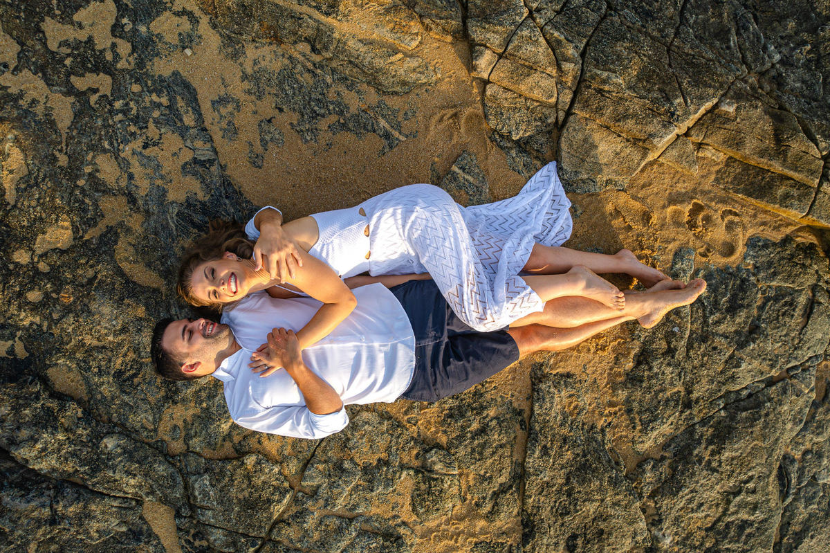 foto de drone de Casal deitado sobre as pedras durante ensaio pré-wedding ao amanhecer em Balneário Camboriú – SC