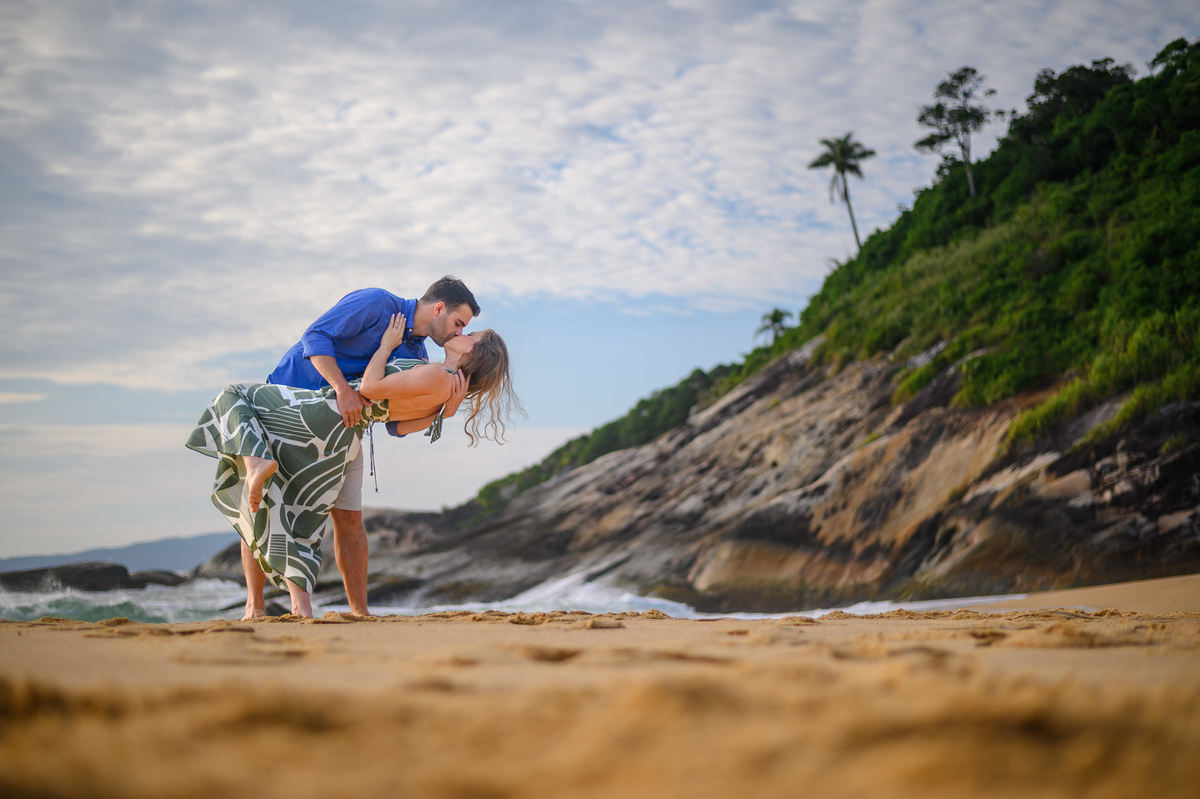 Casal se beijando na praia com pedras ao fundo em ensaio pré-wedding em Balneário Camboriú – SC