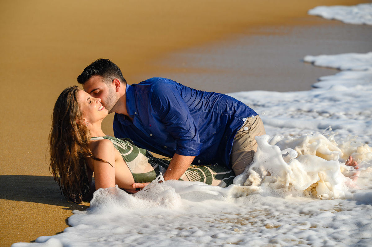 Casal se beijando enquanto ondas molham a areia durante ensaio pré-wedding em Balneário Camboriú – SC