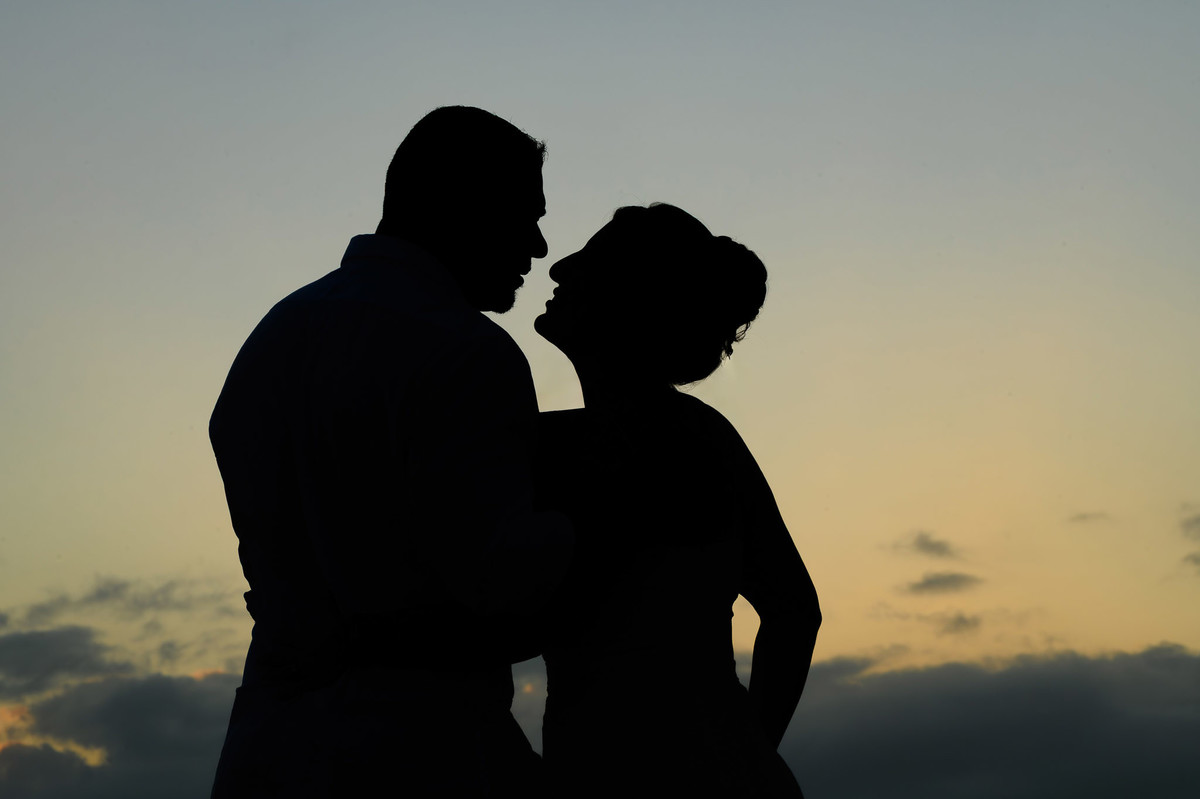 Silhueta de casal se beijando ao amanhecer na praia, ensaio romântico com céu claro em Balneário Camboriú