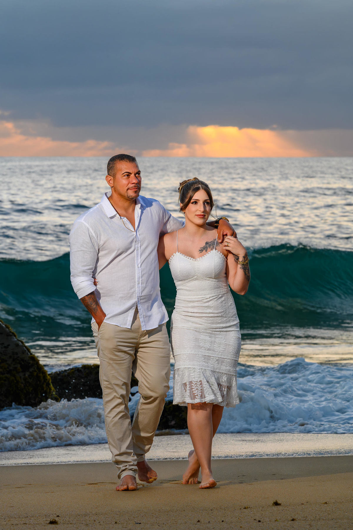 Casal caminhando abraçado na praia do Estaleirinho ao amanhecer, ensaio de casal com mar ao fundo em Santa Catarina