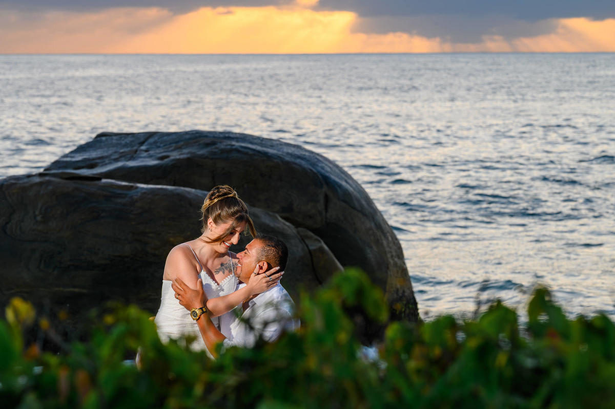 Casal sentado sobre as pedras na praia do Estaleirinho ao amanhecer, ensaio de casal com luz natural suave