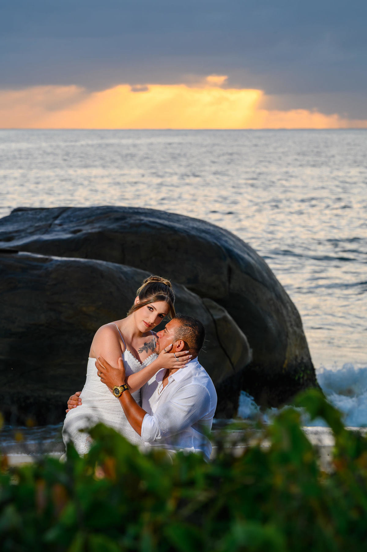 Casal sentado sobre as pedras na praia do Estaleirinho ao amanhecer, ensaio de casal com luz natural suave