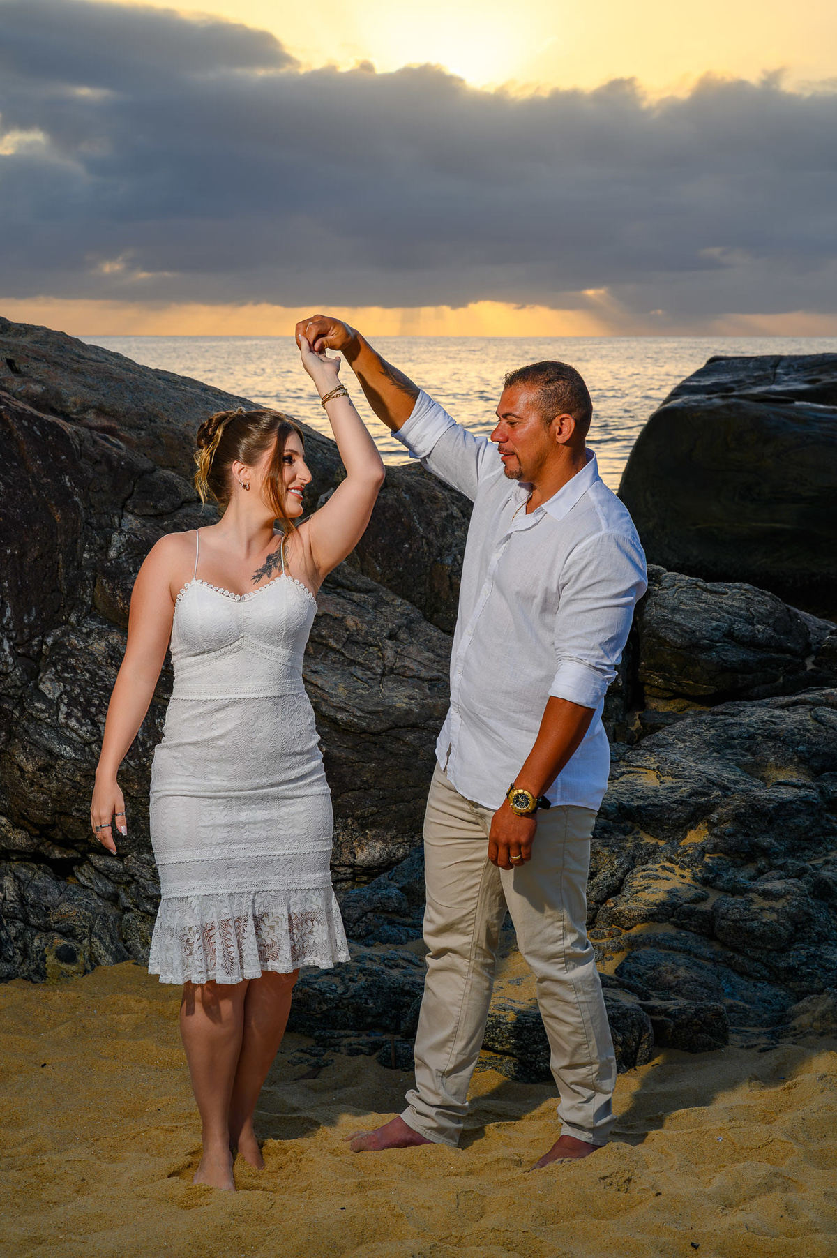 Casal dançando nas pedras da praia durante ensaio de casal ao amanhecer em Balneário Camboriú