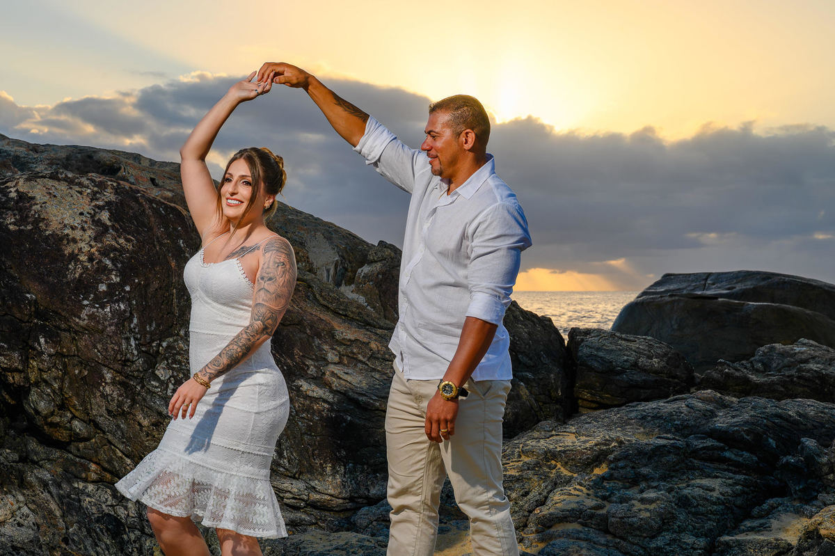 Casal dançando nas pedras da praia durante ensaio de casal ao amanhecer em Balneário Camboriú