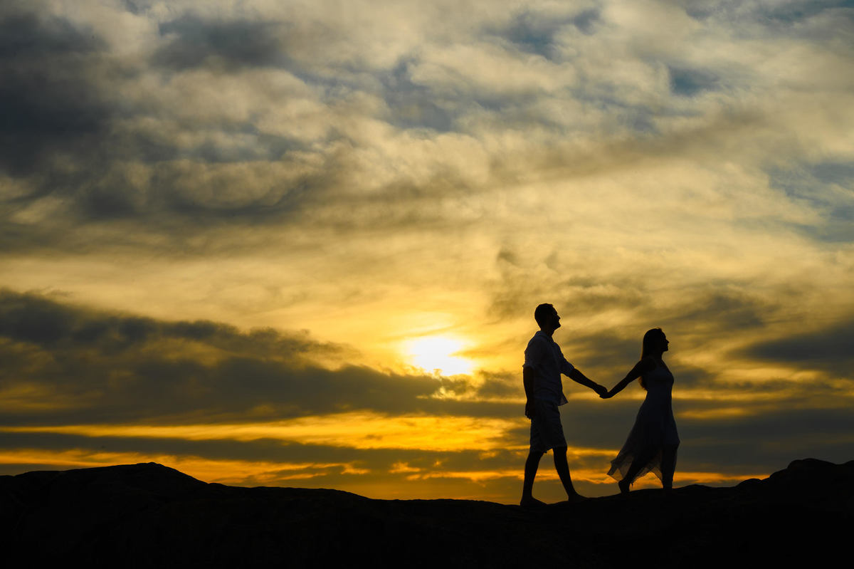 Casal de mãos dadas no topo das pedras durante ensaio pré-wedding ao amanhecer no Estaleirinho