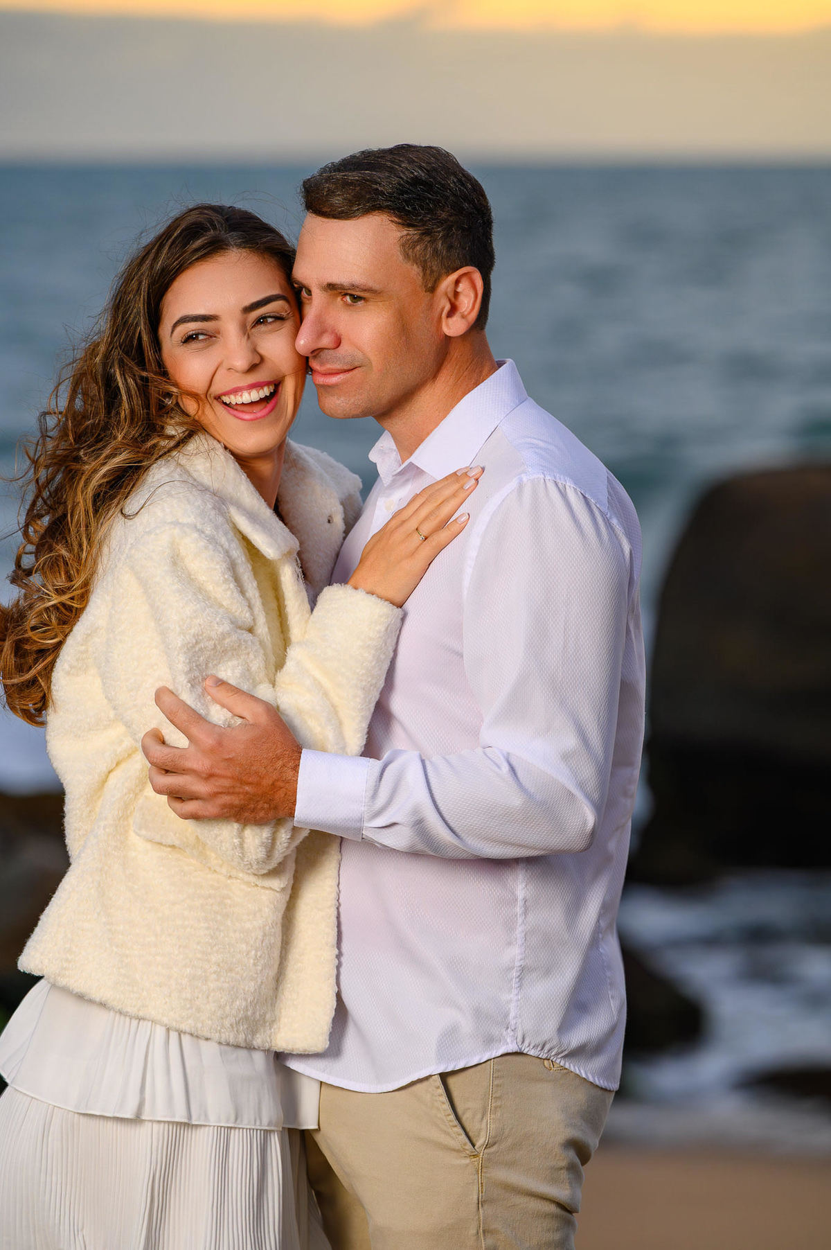 Ensaio pré-wedding ao amanhecer na Praia do Estaleirinho em Balneário Camboriú SC com casal abraçado diante do mar e das pedras