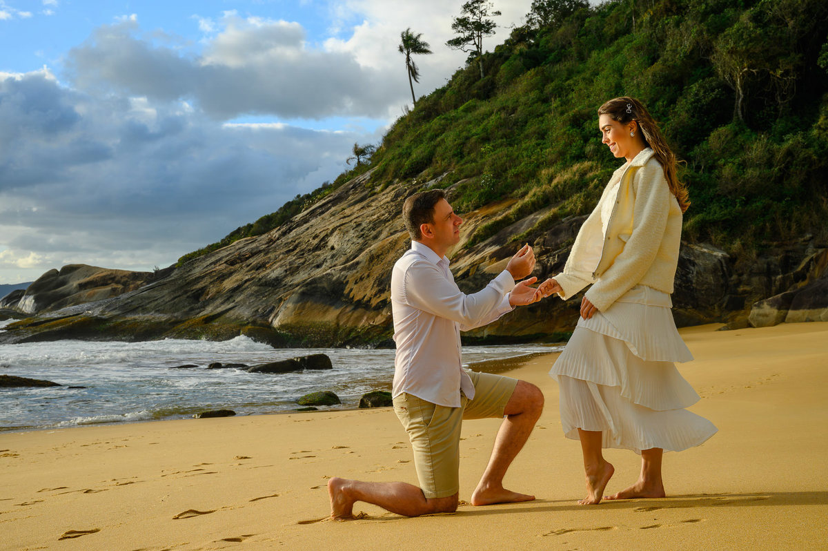 Pedido de casamento encenado durante ensaio pré-wedding na Praia do Estaleirinho em Balneário Camboriú SC com mar ao fundo