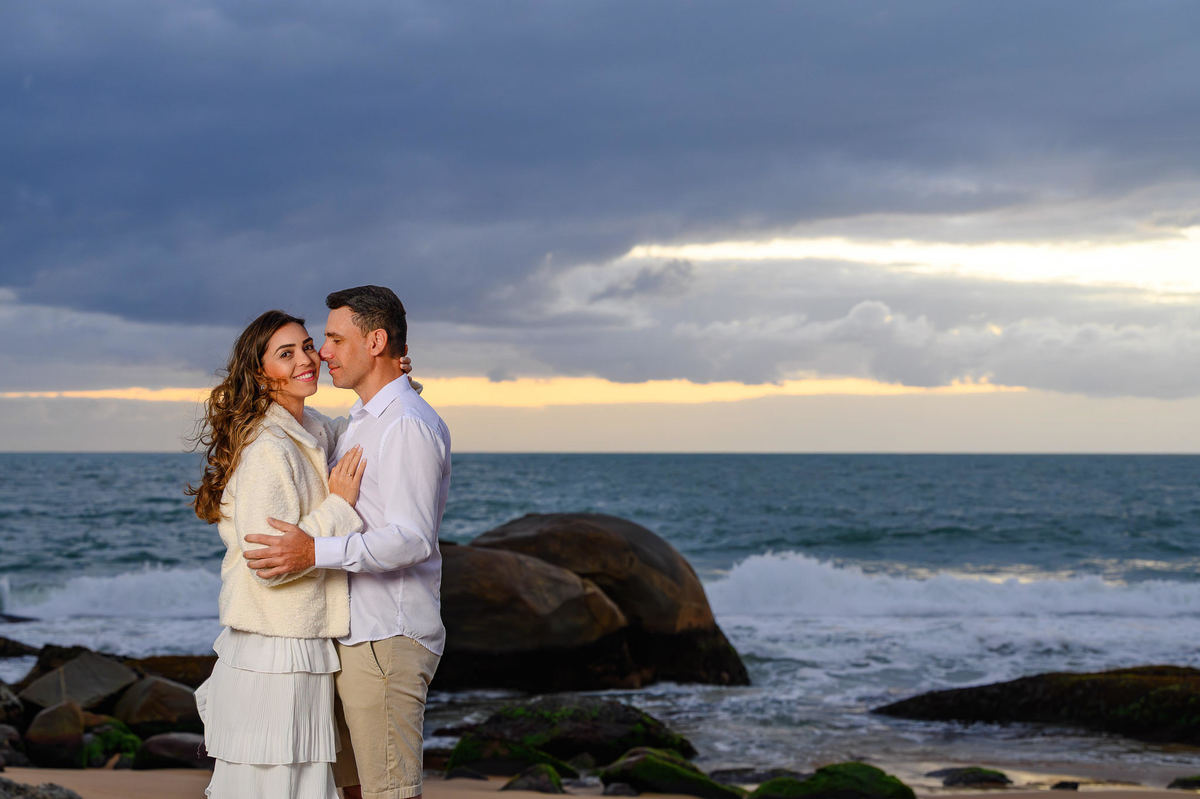 Ensaio pré-wedding ao amanhecer na Praia do Estaleirinho em Balneário Camboriú SC com casal abraçado diante do mar e das pedras