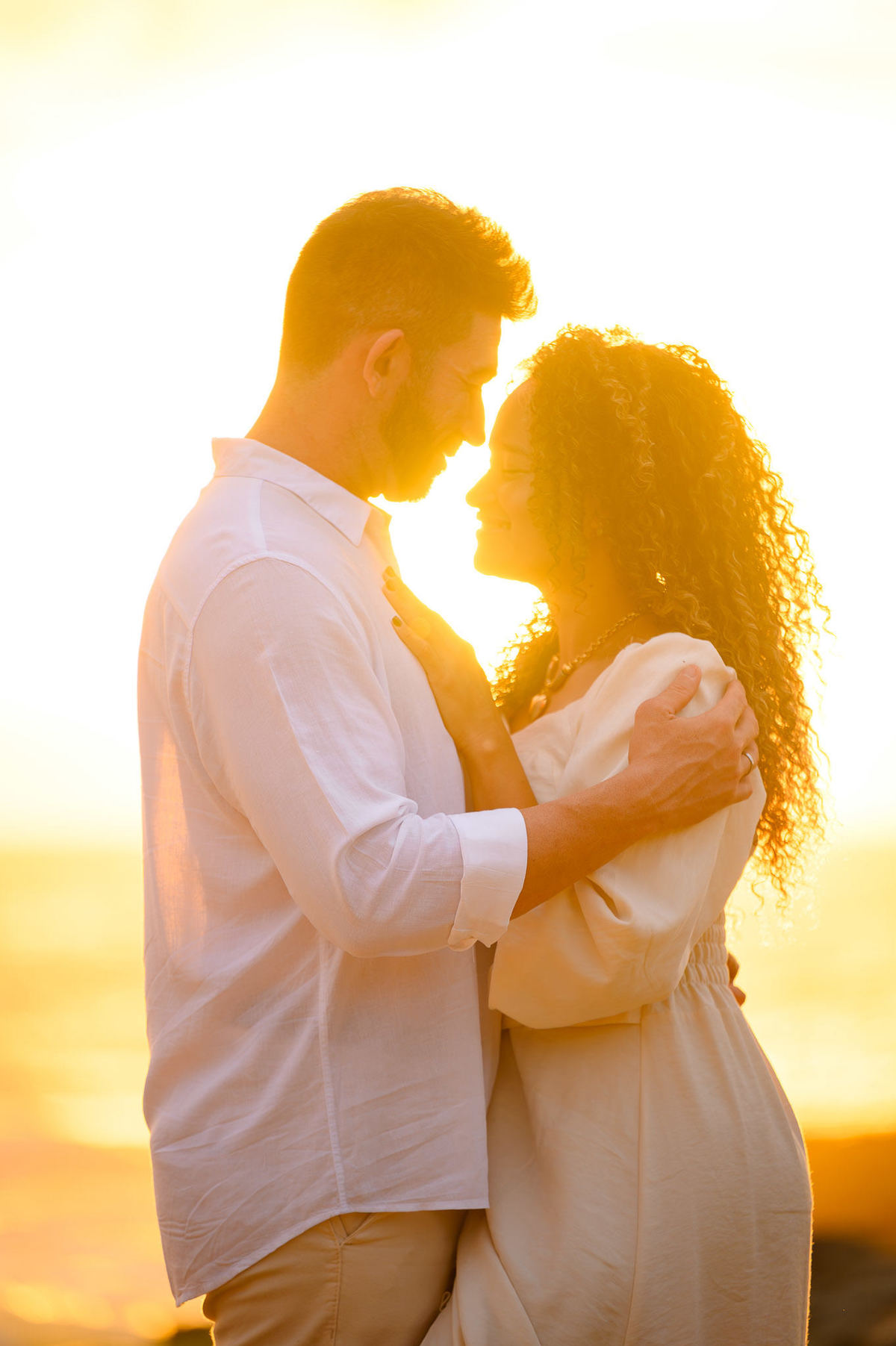 Casal sorrindo durante ensaio fotográfico pré-wedding ao amanhecer na Praia do Estaleirinho com luz dourada do nascer do sol.
