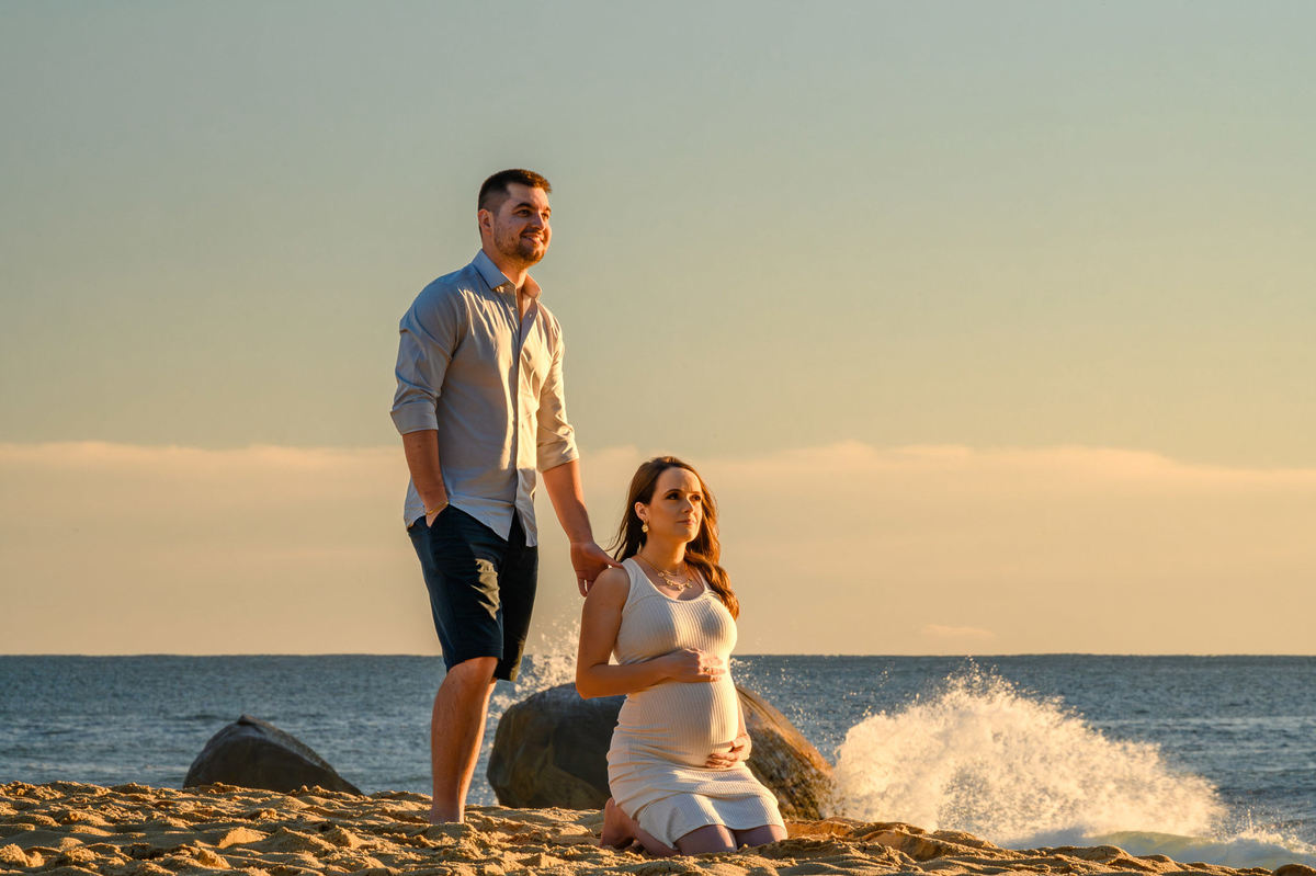 Gestante ajoelhada na areia durante ensaio fotográfico ao amanhecer em Balneário Camboriú SC