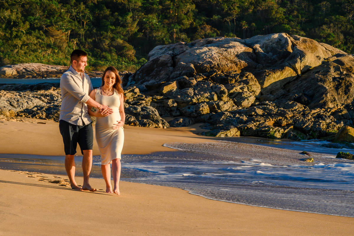 Casal caminhando na praia durante ensaio gestante ao amanhecer em Balneário Camboriú