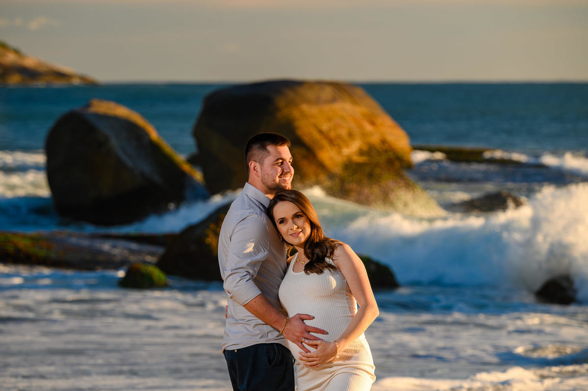 Ensaio gestante ao amanhecer na praia de Balneário Camboriú com pedras e mar ao fundo