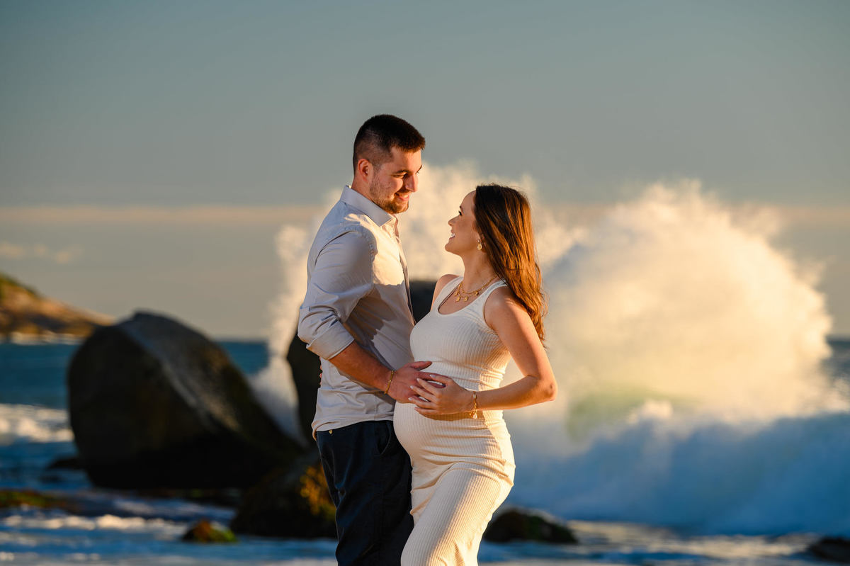 Casal em ensaio fotográfico gestante ao amanhecer com ondas quebrando nas pedras em Balneário Camboriú SC