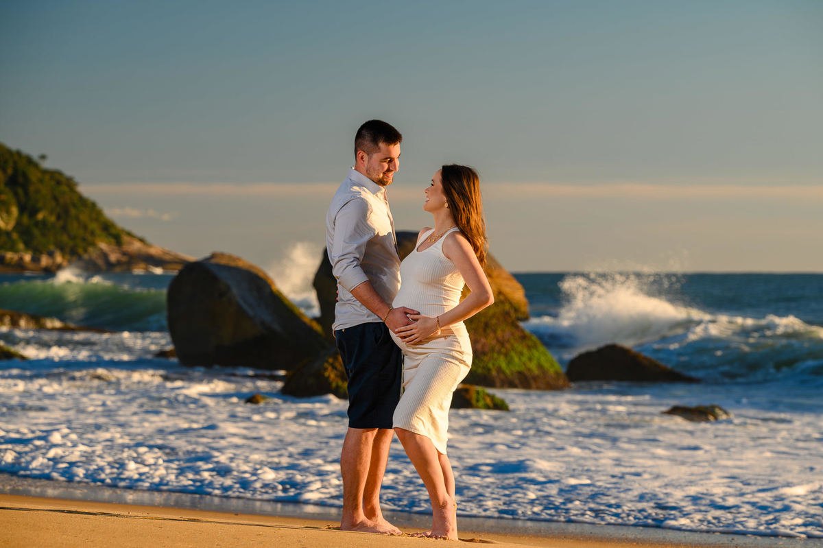 Ensaio gestante ao amanhecer na praia de Balneário Camboriú com pedras e mar ao fundo