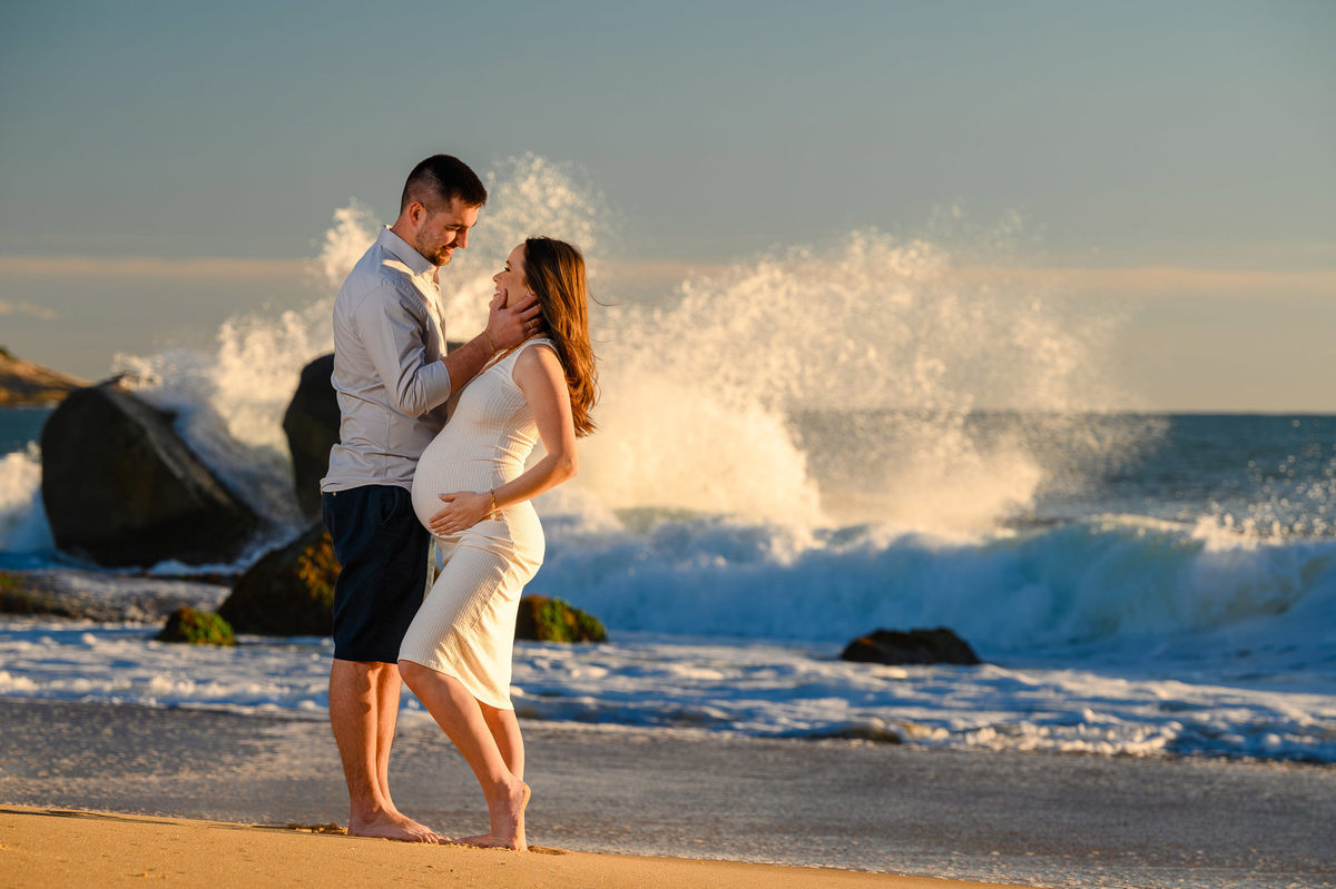 Ensaio gestante ao amanhecer na praia de Balneário Camboriú com pedras e mar ao fundo