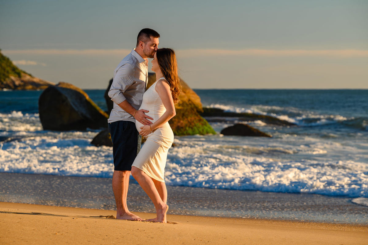 Ensaio gestante ao amanhecer na praia de Balneário Camboriú com pedras e mar ao fundo