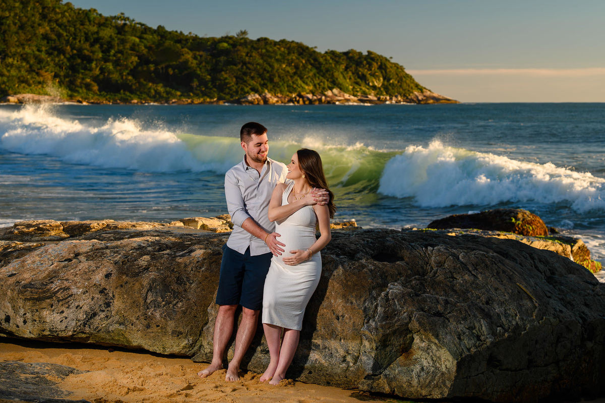 Casal em ensaio gestante ao amanhecer na praia de Balneário Camboriú com ondas ao fundo