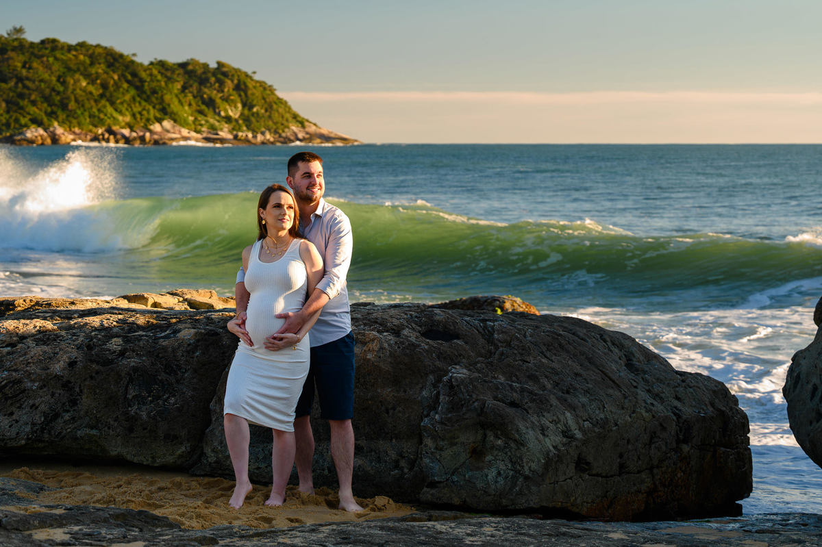 Casal em ensaio gestante ao amanhecer na praia de Balneário Camboriú com ondas ao fundo