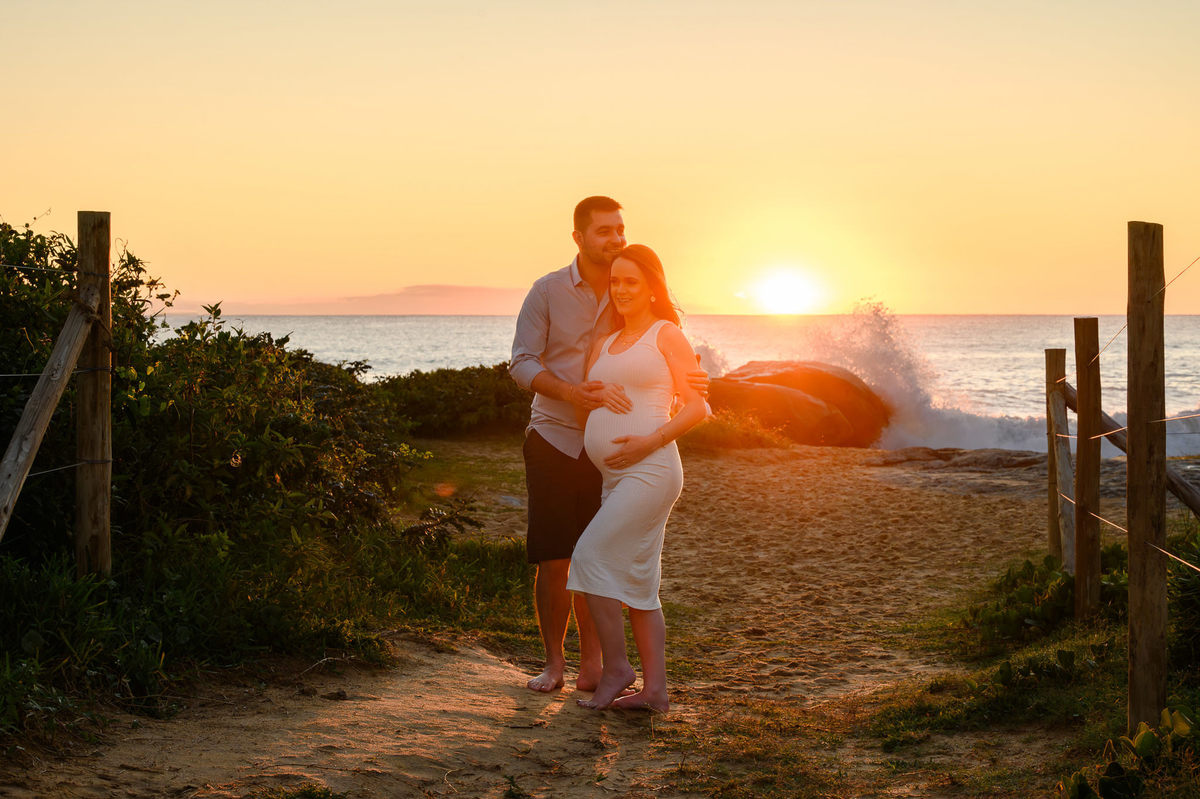 Casal em ensaio gestante ao amanhecer na praia de Balneário Camboriú SC com o sol nascendo ao fundo