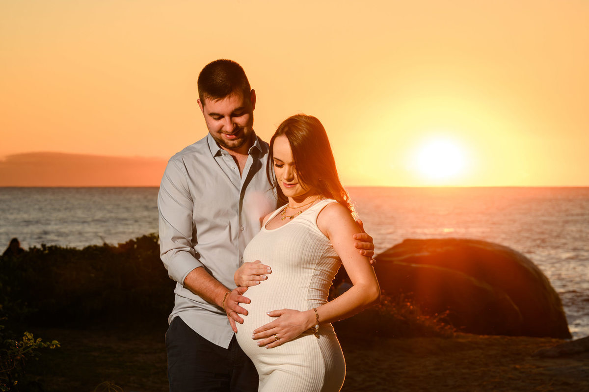 Casal em ensaio gestante ao amanhecer na praia de Balneário Camboriú SC com o sol nascendo ao fundo