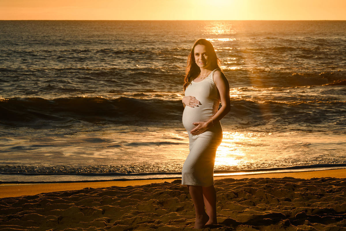 Gestante em ensaio ao amanhecer na praia de Balneário Camboriú com luz dourada do nascer do sol