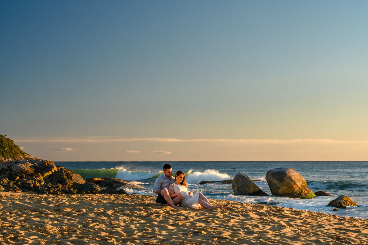 Ensaio gestante ao amanhecer na praia de Balneário Camboriú com pedras e mar ao fundo
