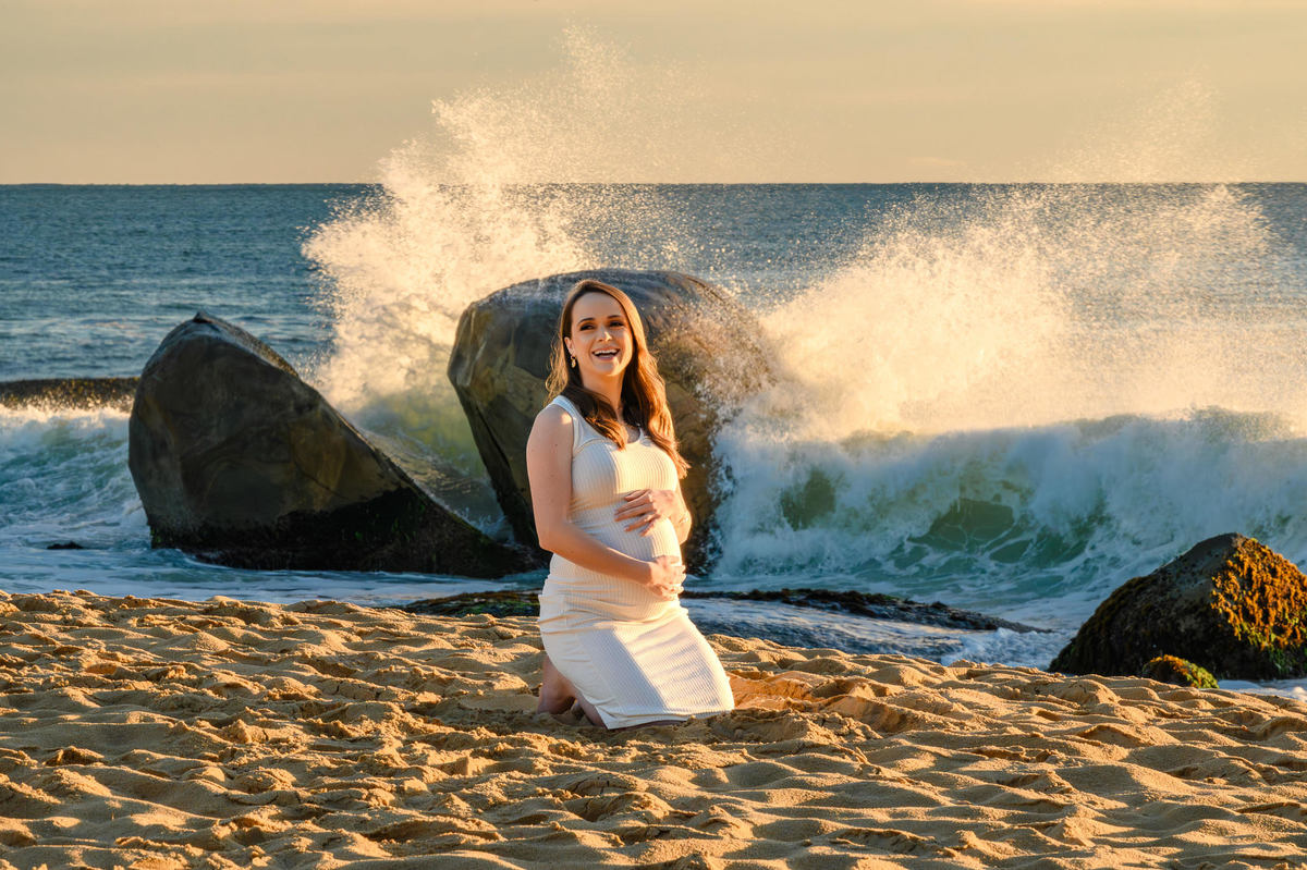 Gestante ajoelhada na areia durante ensaio fotográfico ao amanhecer em Balneário Camboriú SC