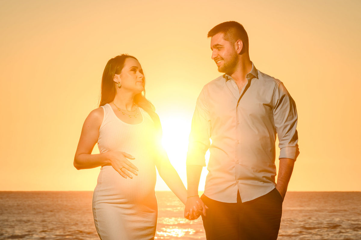 Ensaio fotográfico gestante ao amanhecer em Balneário Camboriú com casal abraçado e luz do nascer do sol