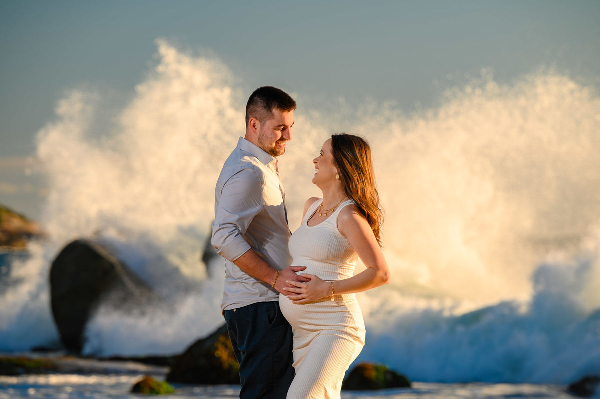 Casal em ensaio fotográfico gestante ao amanhecer com ondas quebrando nas pedras em Balneário Camboriú SC