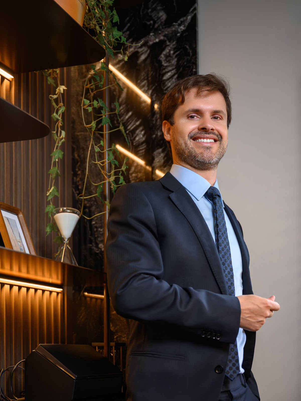 Retrato profissional em ambiente corporativo com estante e elementos decorativos, transmitindo credibilidade e sofisticação.