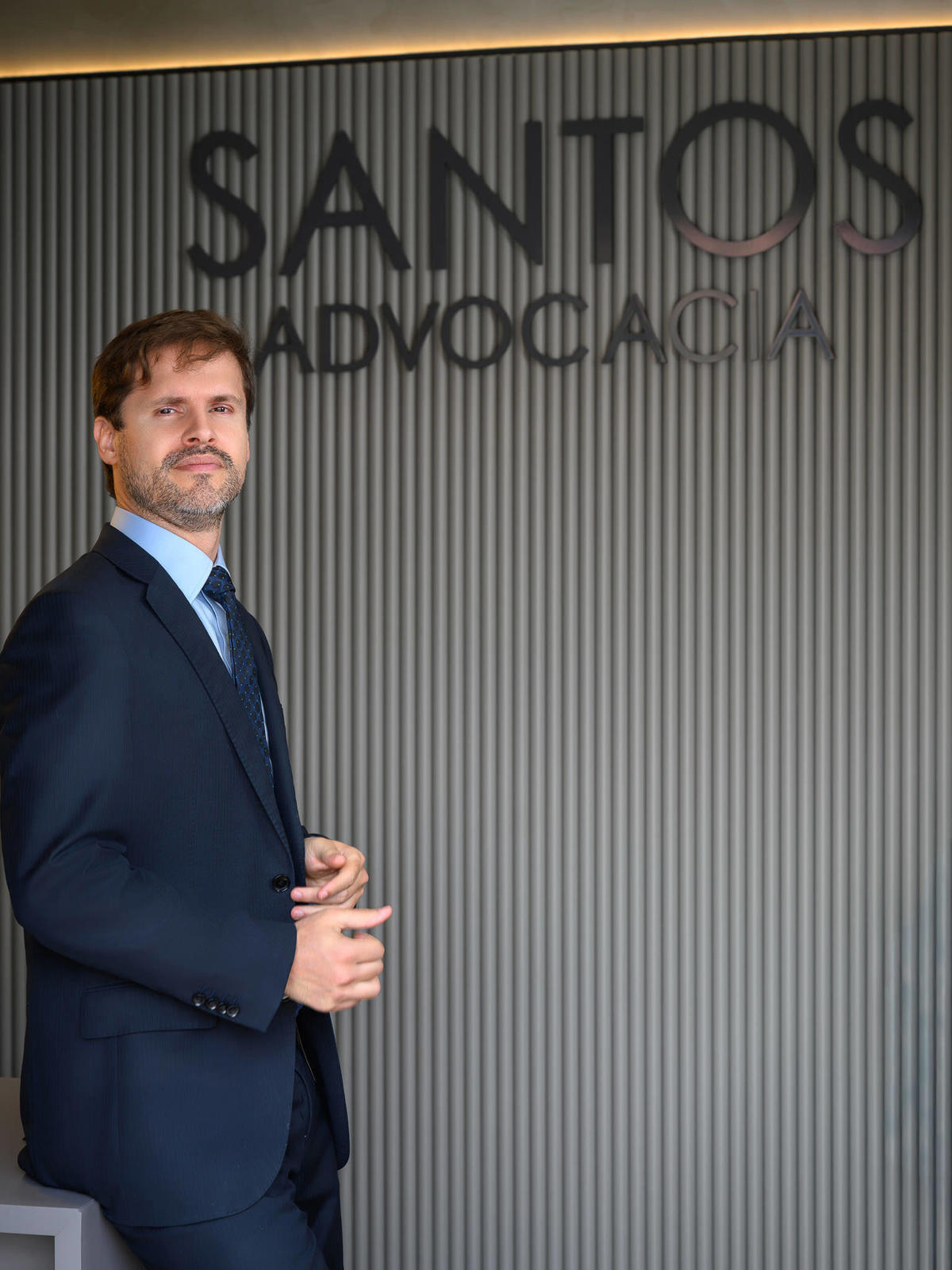 Retrato corporativo de profissional em frente a parede com identidade visual de escritório, reforçando autoridade e presença profissional.