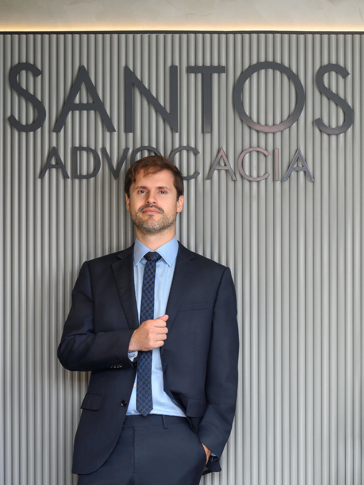 Retrato corporativo de executivo ajustando o paletó em escritório moderno, reforçando imagem de posicionamento profissional.