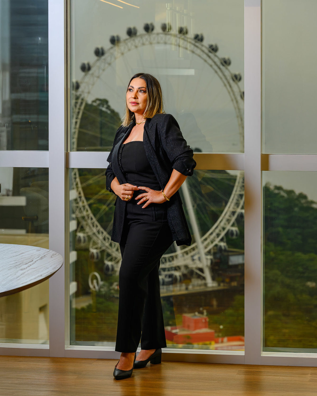 Retrato corporativo de corretora em pé ao lado de janela com vista para a roda-gigante de Balneário Camboriú, em apartamento de alto padrão.